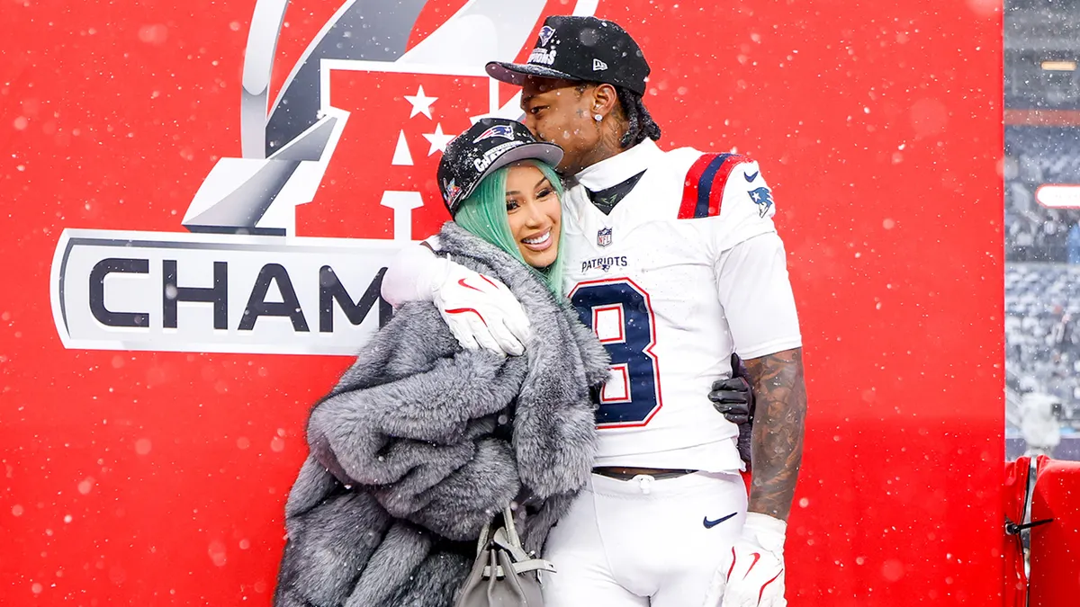 Cardi B and Stefon Diggs share a celebratory embrace on the field, with Diggs in a football uniform and snow falling around them after a championship moment. Cardi B Stefon Diggs Backlash
